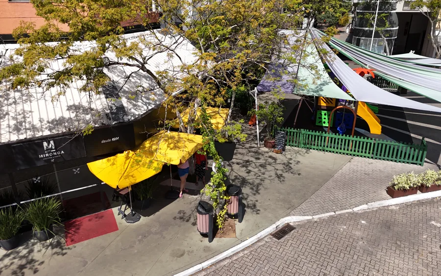 Vista da fachada do Mironga com as mesas na calçada e o parquinho cercado bem em frente