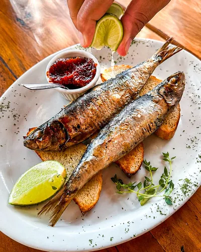 Sardinha portuguesa grelhada sobre torradas, com limão e geleia de pimenta